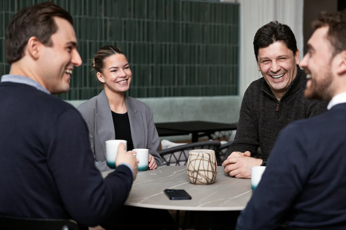Tre kolleger prater over kaffe rundt et bord på jobben