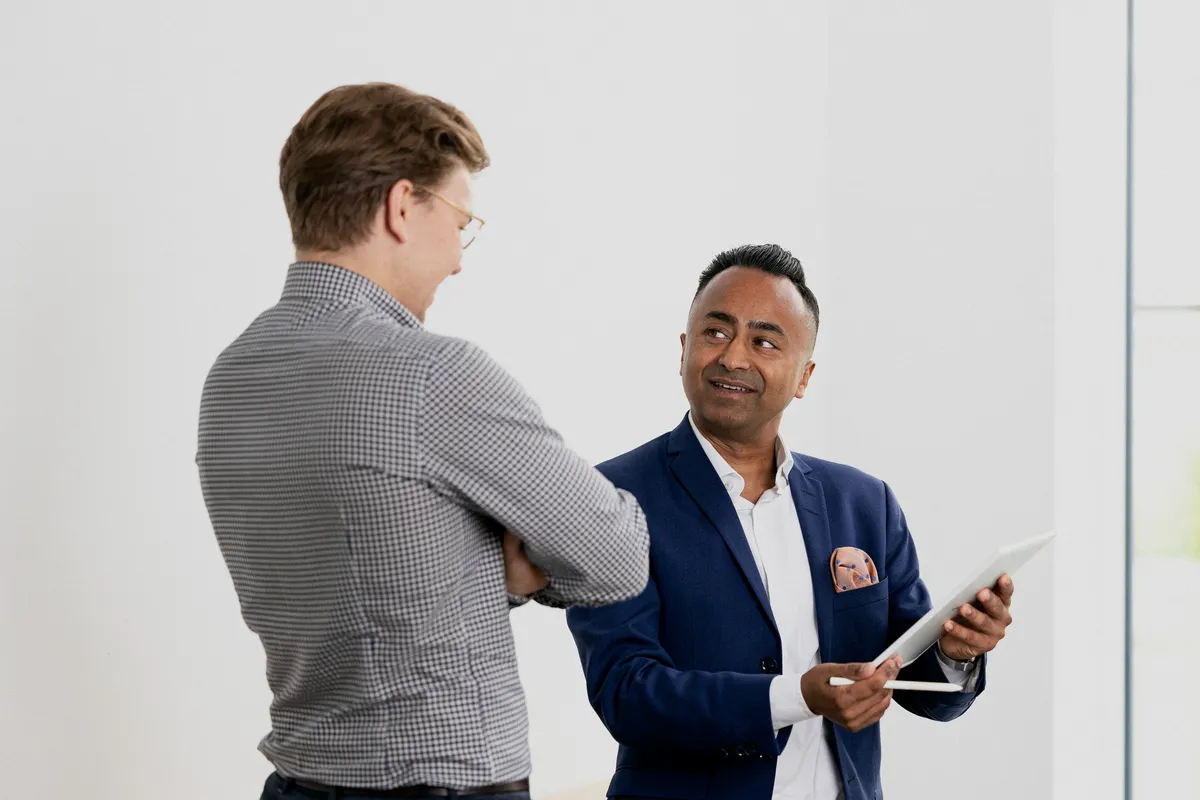 To kolleger ler i samtale, den ene holder en mobiltelefon