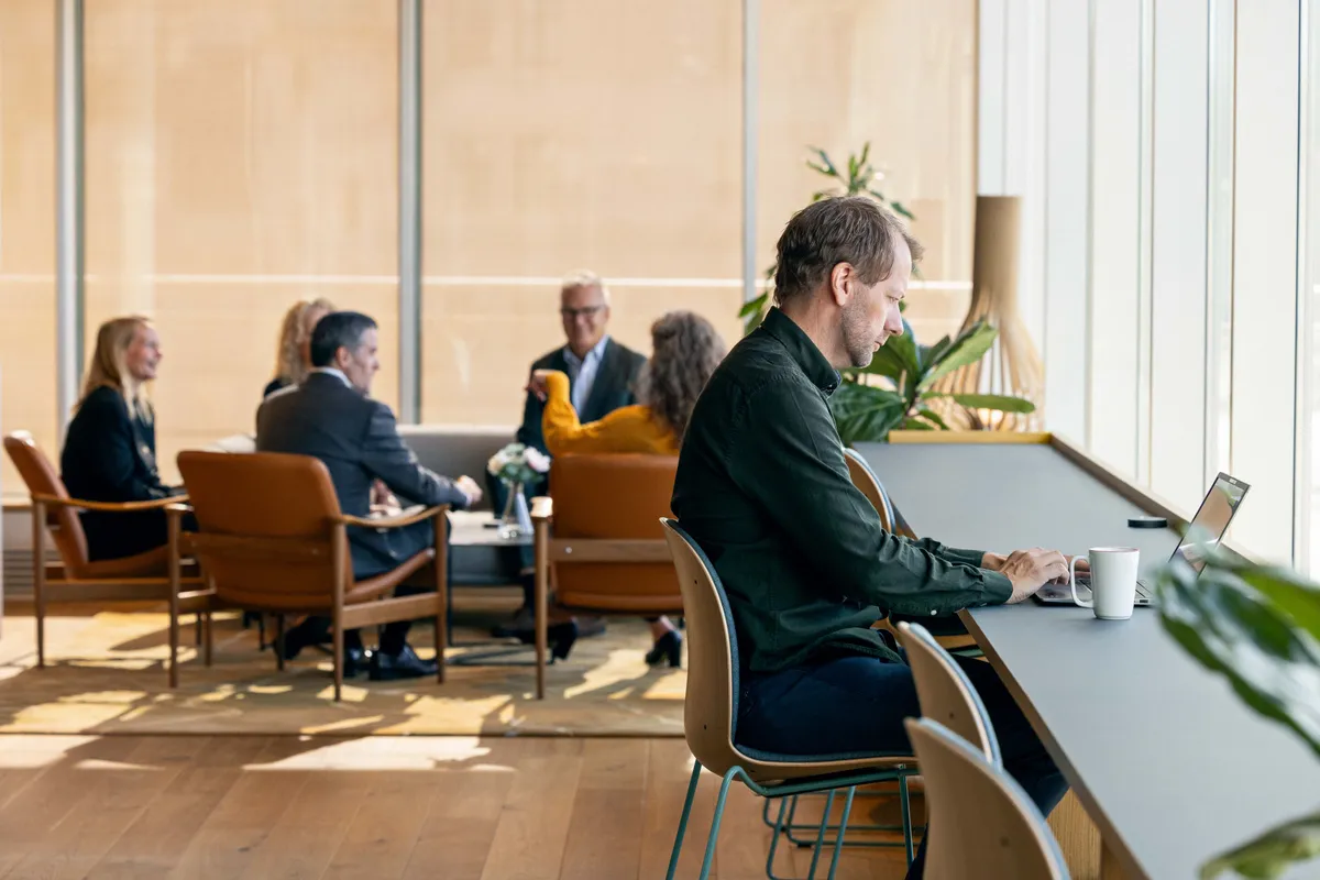Medarbeidere jobber ved et langbord i lyst, åpent kontorlandskap