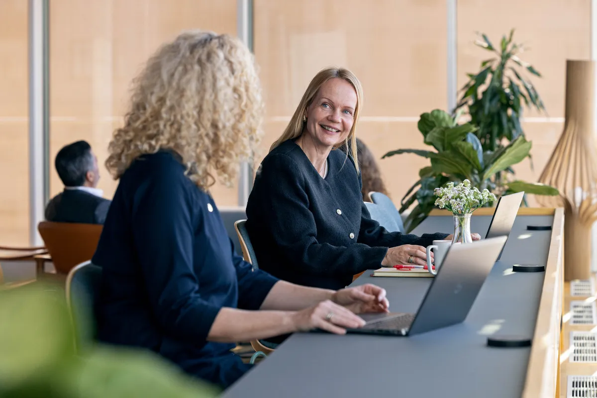 Tre smilende kvinner jobber sammen med laptoper ved et bord