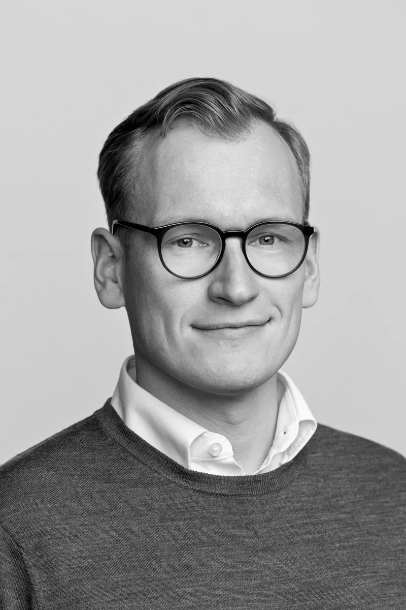 Mannlig ansatt med briller og genser, rolig sort-hvitt studioportrett